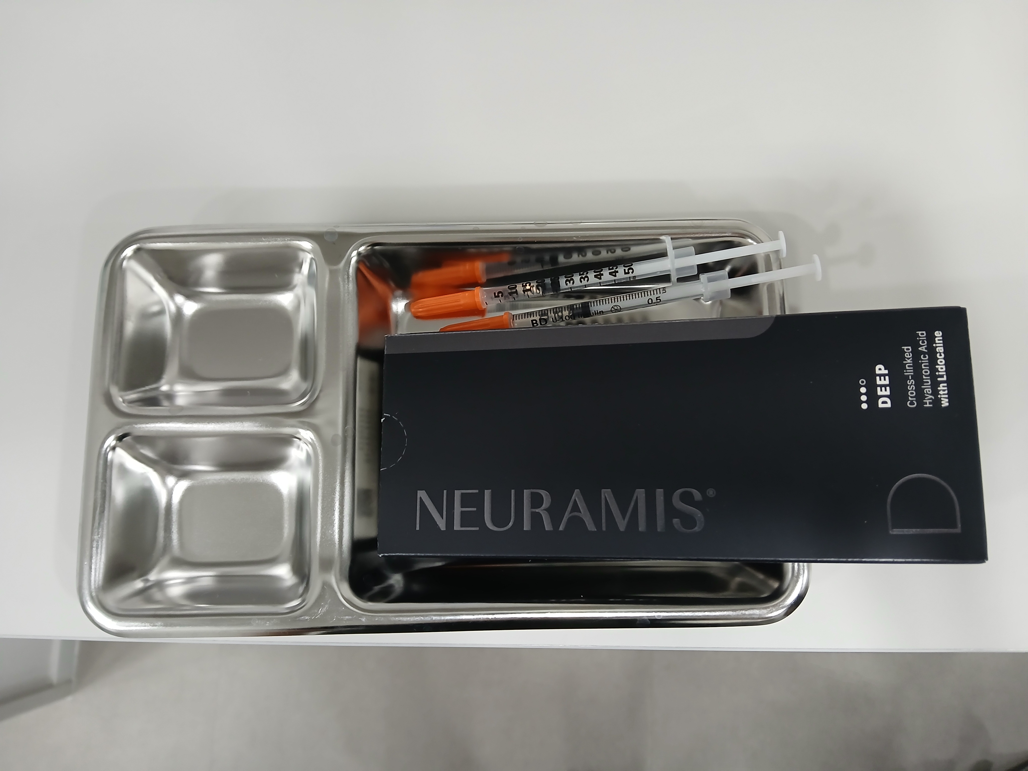 금속 의료용 트레이 위에 필러 제품인 뉴라미스 딥(NEURAMIS DEEP) 박스와 여러 개의 주사기가 위생적으로 준비되어 있는 모습입니다.
